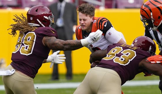 Cincinnati Bengals quarterback Joe Burrow (9) looses his helmet as he is tackled by Washington Football Team defensive tackle Jonathan Allen (93) and defensive end Chase Young (99), during the first half of an NFL football game, Sunday, Nov. 22, 2020, in Landover. (AP Photo/Susan Walsh)