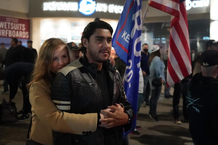A couple hugs Saturday, Nov. 21, 2020 during a protest against a stay-at-home order amid the COVID-19 pandemic in Huntington Beach, Calif. California health officials are restricting overnight activities starting Saturday night, though there are plenty of exceptions. They're calling it a limited stay-at-home order designed to stem the rapidly spreading coronavirus by discouraging social gatherings. (AP Photo/Marcio Jose Sanchez)