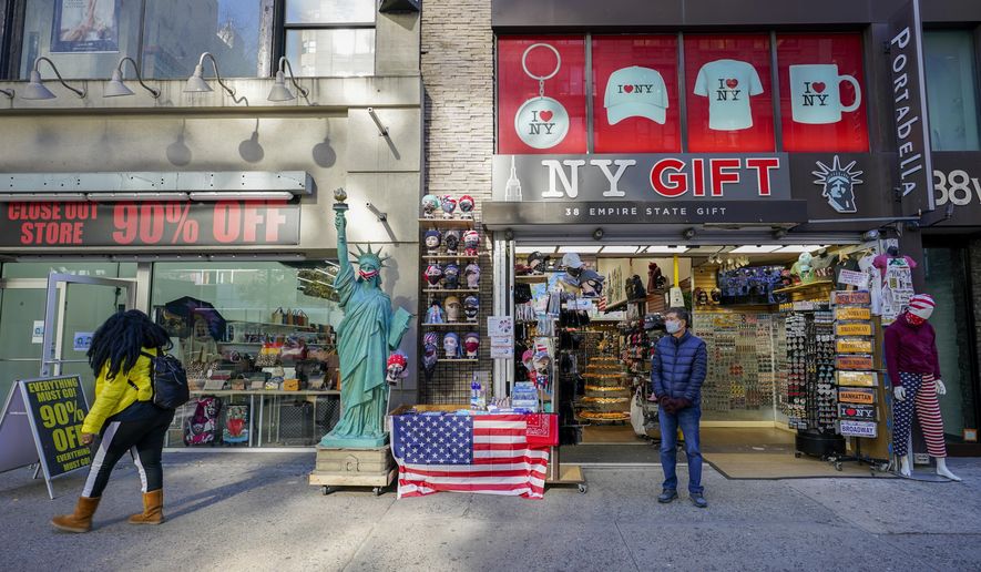 A shop keeper at a gift shop along 34th Street stands on the sidewalk waiting for customers, Friday, Nov. 20, 2020, in New York. In souvenir shops from Times Square to the World Trade Center, shelves full of T-shirts and trinkets still love New York, as the slogan goes. But the proprietors wonder when their customers will, again. The coronavirus has altered many aspects of life and business in the United States&#39; biggest city, and the pandemic is taking a major toll on the gifts-and-luggage stores that dot tourist-friendly areas. After setting records year after year since 2010, travel to New York has plummeted during the pandemic. (AP Photo/Mary Altaffer)
