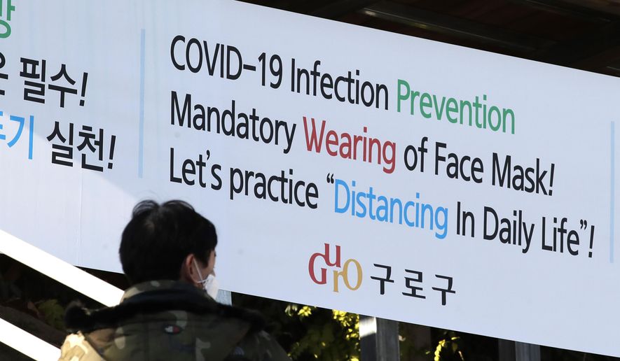 A man wearing a face mask walks by a banner showing precautions against the coronavirus in Seoul, South Korea, Monday, Nov. 23, 2020. (AP Photo/Lee Jin-man)