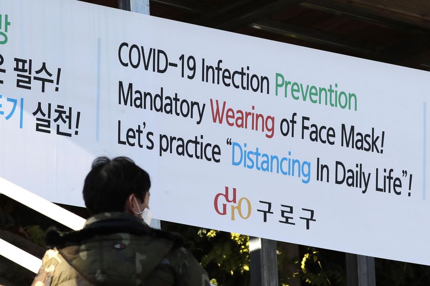 A man wearing a face mask walks by a banner showing precautions against the coronavirus in Seoul, South Korea, Monday, Nov. 23, 2020. (AP Photo/Lee Jin-man)