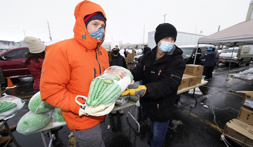 Chad MacKenzie, right, hands a frozen turkey to Mike Brumbaugh, both volunteers from Vail, Colo., to give to a motorist as part of a "Banquet in a Box" from the Denver Rescue Mission as the Thanksgiving Day feasts are distributed in a parking lot at Empower Field at Mile High early Tuesday, Nov. 24, 2020, in Denver. More than 3,000 of the boxes filled with the ingredients for a traditional Thanksgiving dinner were handed out through the rescue mission and the Denver Broncos. (AP Photo/David Zalubowski)
