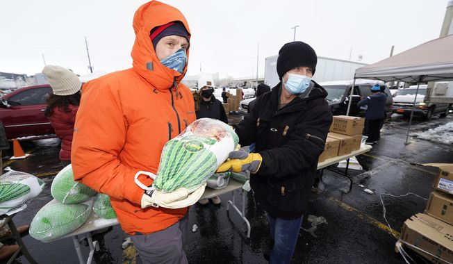 Chad MacKenzie, right, hands a frozen turkey to Mike Brumbaugh, both volunteers from Vail, Colo., to give to a motorist as part of a "Banquet in a Box" from the Denver Rescue Mission as the Thanksgiving Day feasts are distributed in a parking lot at Empower Field at Mile High early Tuesday, Nov. 24, 2020, in Denver. More than 3,000 of the boxes filled with the ingredients for a traditional Thanksgiving dinner were handed out through the rescue mission and the Denver Broncos. (AP Photo/David Zalubowski)
