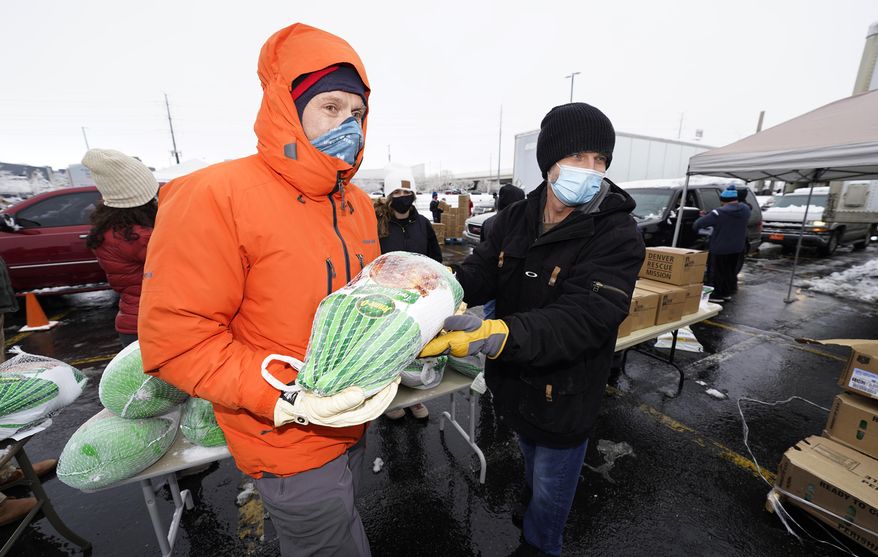 Chad MacKenzie, right, hands a frozen turkey to Mike Brumbaugh, both volunteers from Vail, Colo., to give to a motorist as part of a &amp;quot;Banquet in a Box&amp;quot; from the Denver Rescue Mission as the Thanksgiving Day feasts are distributed in a parking lot at Empower Field at Mile High early Tuesday, Nov. 24, 2020, in Denver. More than 3,000 of the boxes filled with the ingredients for a traditional Thanksgiving dinner were handed out through the rescue mission and the Denver Broncos. (AP Photo/David Zalubowski)