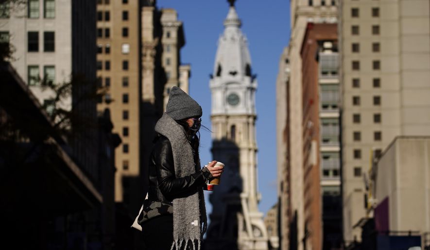 In this Nov. 18, 2020 photo, a person wearing a face mask crosses Broad Street in Philadelphia. As governors and mayors grapple with an out-of-control pandemic, they are ratcheting up mask mandates and imposing restrictions on small indoor gatherings, which have been blamed for accelerating the spread of the coronavirus. (AP Photo/Matt Slocum)