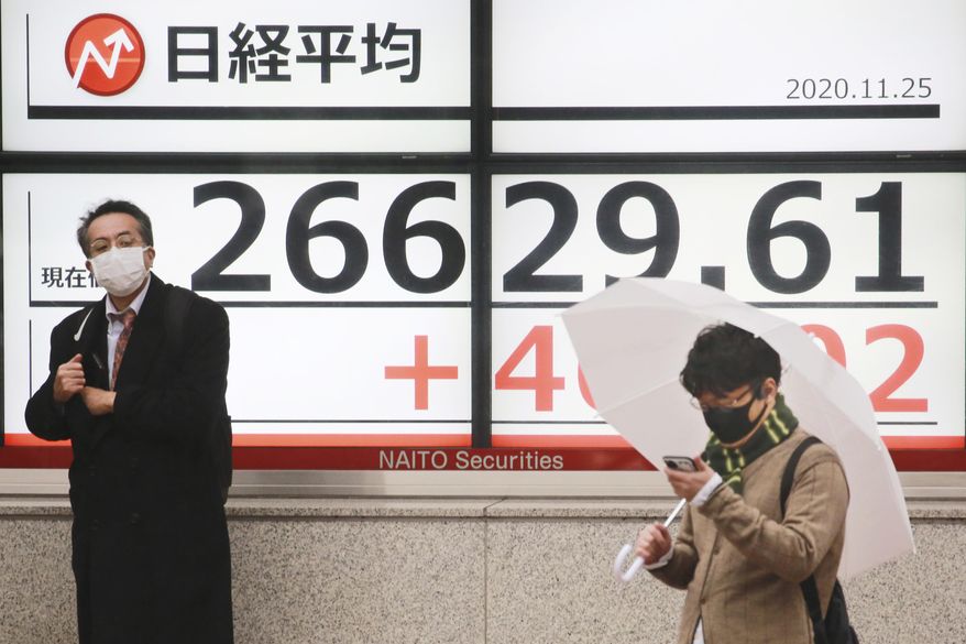 People stand by an electronic stock board of a securities firm showing Japan's Nikkei 225 index in Tokyo, Wednesday, Nov. 25, 2020. Asian shares rose Wednesday after the Dow Jones Industrial Average closed above 30,000 points for the first time despite an ongoing pandemic, as progress in development of coronavirus vaccines kept investors in a buying mood. (AP Photo/Koji Sasahara)