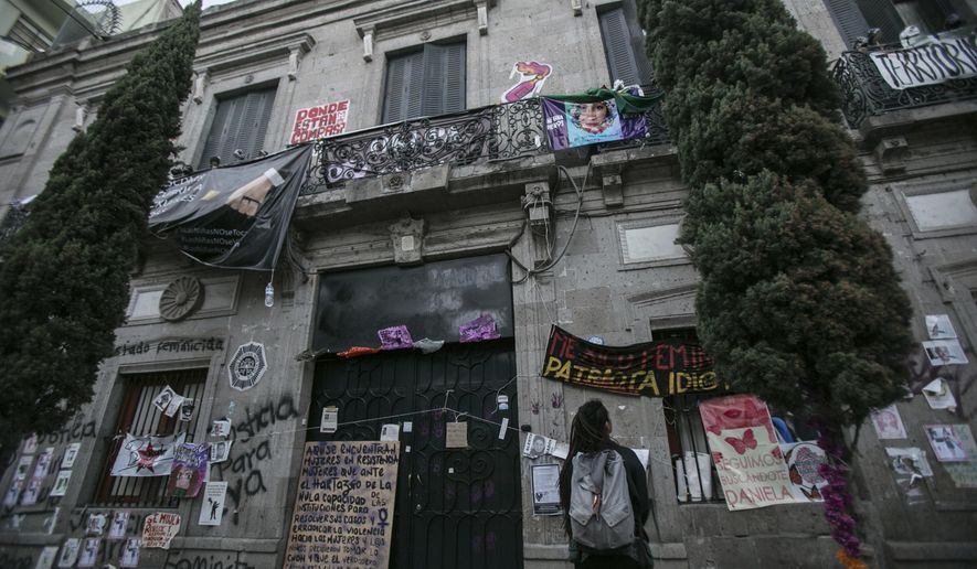 A woman looks at the Mexico’s Human Rights Commission (CNDH) headquarters which has been occupied for almost three months by women’s rights activists who have converted it into a refuge for victims of gender violence in Mexico City, Tuesday, Nov. 17, 2020. Feminist activists are occupying the building to demand justice for the victims of sexual abuse, femicide, and other gender violence, and are hosting some women and their children after the government either failed to solve or investigate sexual attacks on their guest’s daughters. (AP Photo/Ginnette Riquelme)