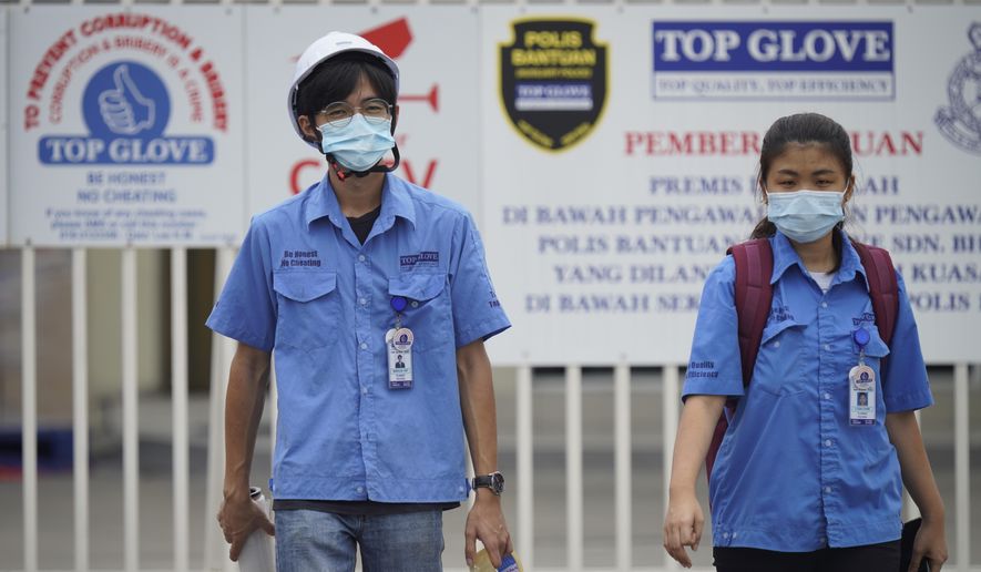 Workers from Top Glove walk out from Top Glove factory in Shah Alam, Malaysia, Wednesday, Nov. 25, 2020. Malaysia's Top Glove Corp., the world's largest maker of rubber gloves, says it expects a two to four-week delay in deliveries after more than 2,000 workers at its factories were infected by the coronavirus, raising the possibility of supply disruptions during the pandemic. (AP Photo/Vincent Thian)