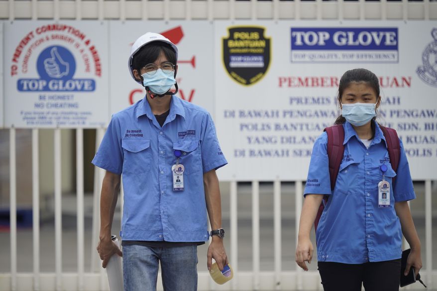 Workers from Top Glove walk out from Top Glove factory in Shah Alam, Malaysia, Wednesday, Nov. 25, 2020. Malaysia's Top Glove Corp., the world's largest maker of rubber gloves, says it expects a two to four-week delay in deliveries after more than 2,000 workers at its factories were infected by the coronavirus, raising the possibility of supply disruptions during the pandemic. (AP Photo/Vincent Thian)