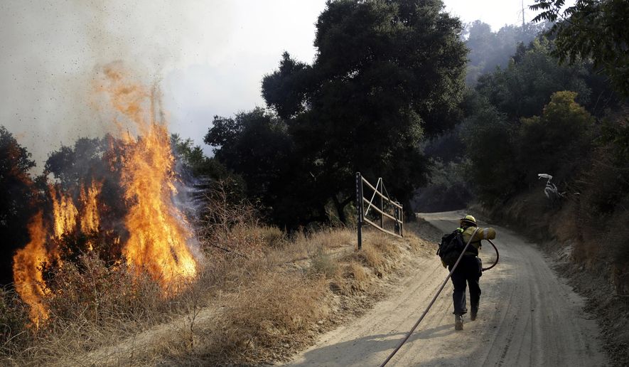 FILE - In this Oct. 12, 2019, file photo, a firefighter runs up a fire road to hose down flames from a wildfire in Newhall, Calif. Thousands of people in Southern California lost power Thanksgiving Day after a utility began shutting off electricity to prevent wildfires from being ignited by damage to power lines amid strong winds. At least 3,000 customers in Los Angeles and Ventura counties lost electricity Thursday, Nov. 26, 2020 and more than 100,000 other customers are at risk of losing power, according to Southern Edison.(AP Photo/Marcio Jose Sanchez, File)