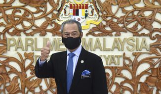 In this photo released by Malaysia&#39;s Information Ministry, Prime Minister Muhyiddin Yassin poses for a picture at the parliament, in Kuala Lumpurf, Malaysia Thursday, Nov. 26, 2020. Malaysia&#39;s Parliament Thursday approved the government&#39;s proposed 2021 budget, throwing a political lifeline to embattled Prime Minister Muhyiddin Yassin amid strong resistance to his nine-month-old leadership. (Zarith Zulkifli/Malaysia&#39;s Department of Information via AP)
