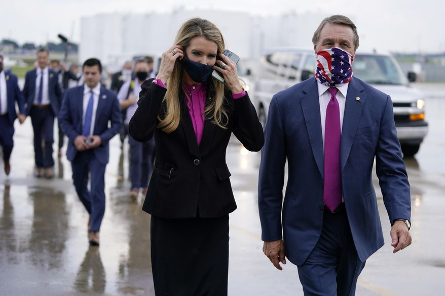 In this July 15, 2020, file photo Sen. Kelly Loeffler, R-Ga., puts on a face mask as she walks with Sen. David Perdue, R-Ga., right, at UPS Hapeville Airport Hub in Atlanta. (AP Photo/Evan Vucci, File)