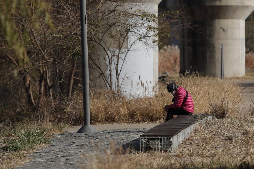 A woman wearing a face mask as a precaution against the coronavirus, sits on a bench while maintaining social distancing at a park in Seoul, South Korea, Thursday, Nov. 26, 2020. (AP Photo/Lee Jin-man)