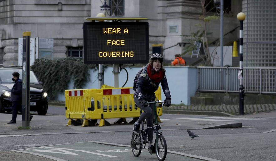 A woman cycles on a Brompton folding bicycle past a sign outside Waterloo Station reminding people they are required to wear face coverings inside the station and whilst traveling on trains, in London, during England&#39;s second coronavirus lockdown, Friday, Nov. 20, 2020. (AP Photo/Matt Dunham)