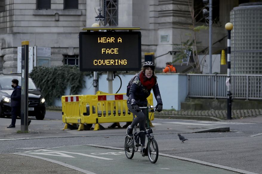 A woman cycles on a Brompton folding bicycle past a sign outside Waterloo Station reminding people they are required to wear face coverings inside the station and whilst traveling on trains, in London, during England&#x27;s second coronavirus lockdown, Friday, Nov. 20, 2020. (AP Photo/Matt Dunham)
