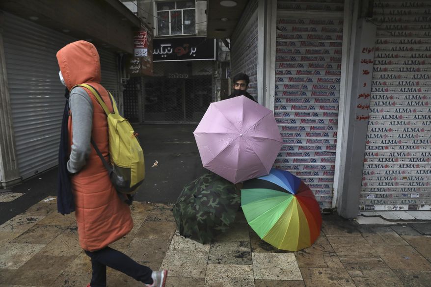 A vendor sells umbrellas outside closed shops in northern Tehran, Iran, Sunday, Nov. 22, 2020. Iran on Saturday shuttered businesses and curtailed travel between its major cities, including the capital of Tehran, as it grapples with the worst outbreak of the coronavirus in the Mideast region. (AP Photo/Vahid Salemi)