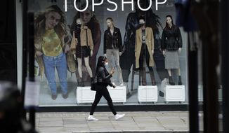 FILE - In this file photo dated Friday, Nov. 20, 2020, a woman wearing a face mask walks past mannequins wearing face masks in the window of a temporarily closed branch of the Topshop women&#39;s clothing chain during England&#39;s second coronavirus lockdown, in London.  Some 15,000 retailing jobs in Britain are in peril after Arcadia Group, owner of some of the country&#39;s best-known fashion chains like Topshop, confirmed Friday Nov. 27, 2020, that it is in talks about its future. (AP Photo/Matt Dunham, FILE)