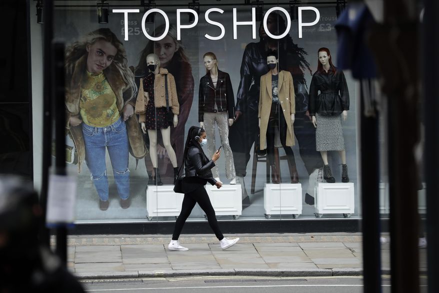 FILE - In this file photo dated Friday, Nov. 20, 2020, a woman wearing a face mask walks past mannequins wearing face masks in the window of a temporarily closed branch of the Topshop women&#39;s clothing chain during England&#39;s second coronavirus lockdown, in London.  Some 15,000 retailing jobs in Britain are in peril after Arcadia Group, owner of some of the country&#39;s best-known fashion chains like Topshop, confirmed Friday Nov. 27, 2020, that it is in talks about its future. (AP Photo/Matt Dunham, FILE)