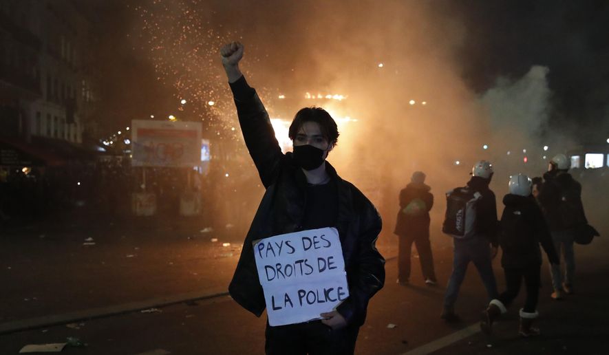 A protester holds a poster reading "Land of rights for the police" during a demonstration against a security law Saturday, Nov. 28, 2020 in Paris. Thousands of critics of a proposed security law that would restrict sharing images of police officers in France gathered across the country in protest, and officers in Paris who were advised to behave responsibly during the demonstrations fired tear gas to disperse rowdy protesters in the largely peaceful crowd. The cause has gained fresh impetus in recent days after footage emerged of French police officers beating up a Black man, triggering a nationwide outcry. (AP Photo/Francois Mori)