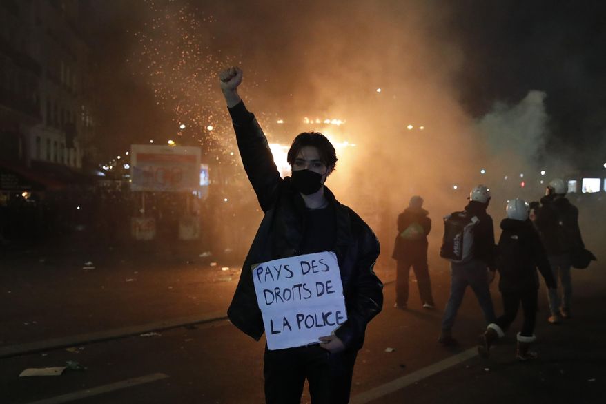 A protester holds a poster reading "Land of rights for the police" during a demonstration against a security law Saturday, Nov. 28, 2020 in Paris. Thousands of critics of a proposed security law that would restrict sharing images of police officers in France gathered across the country in protest, and officers in Paris who were advised to behave responsibly during the demonstrations fired tear gas to disperse rowdy protesters in the largely peaceful crowd. The cause has gained fresh impetus in recent days after footage emerged of French police officers beating up a Black man, triggering a nationwide outcry. (AP Photo/Francois Mori)