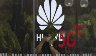 FILE - In this Wednesday, July 15, 2020 file photo, a worker wearing a mask to curb the spread of the coronavirus speaks on the phone near the Huawei logo in a store in Beijing. U.K. telecom companies won&#39;t be allowed to install Huawei equipment in their high-speed 5G networks after September 2021, the British government said Monday Nov. 30, 2020, hardening its line against the Chinese technology company. (AP Photo/Ng Han Guan, File)