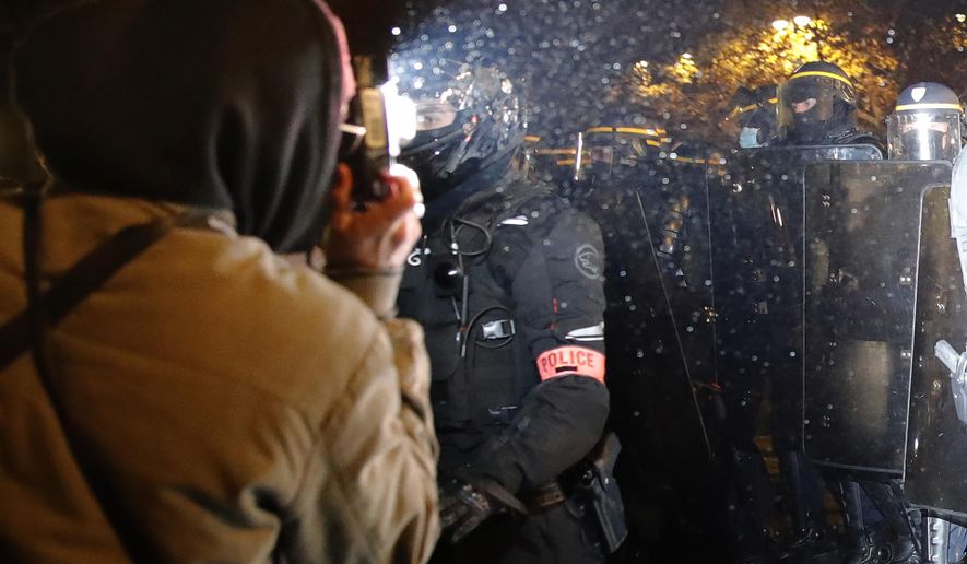 FILE - In this Nov.21, 2020 file photo a demonstrator takes a picture of policemen during a protest against bill on police images, in Paris. As videos helped reveal many cases of police brutality, French civil rights activists voiced fears that a new security law would threaten efforts by people from minorities and poor neighborhoods to document incidents involving law enforcement officers. French President Emmanuel Macron's government is pushing a new security bill that would notably make it illegal to publish images of officers with intent to cause them harm. (AP Photo/Christophe Ena, File)