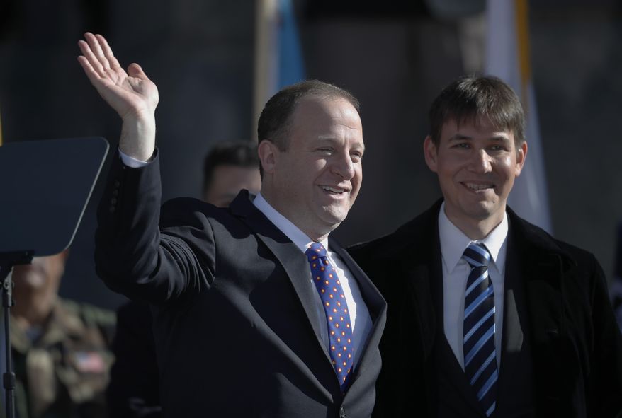 FILE - In this Tuesday, Jan. 8, 2019 file photo, Colorado Gov. Jared Polis, left, joins his partner, Marlon Reis, in acknowledging the crowd after Polis took the oath of office during the inauguration ceremony in Denver. Colorado Gov. Jared Polis has tested positive for the coronavirus. Polis and his partner, Marlon Reis, both have COVID-19 and are asymptomatic, the governor said in a statement Saturday night, Nov. 28, 2020. (AP Photo/David Zalubowski, Pool)