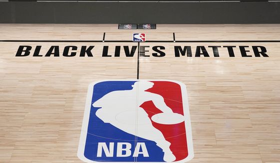 In this Aug. 28, 2020, file photo, Black Lives Matter is displayed near the NBA logo in an empty basketball arena in Lake Buena Vista, Fla. NBA training camps open around the league Tuesday, Dec. 1, 2020, though on-court sessions will be limited to individual workouts and only for those players who have gotten three negative coronavirus test results back in the last few days.   (AP Photo/Ashley Landis, Pool, File)