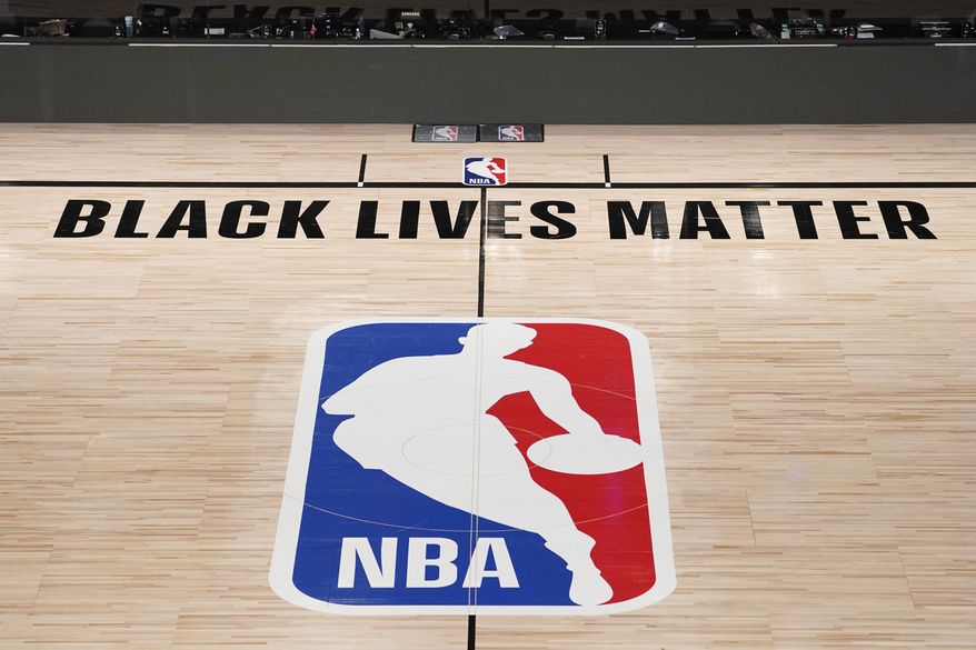 In this Aug. 28, 2020, file photo, Black Lives Matter is displayed near the NBA logo in an empty basketball arena in Lake Buena Vista, Fla. NBA training camps open around the league Tuesday, Dec. 1, 2020, though on-court sessions will be limited to individual workouts and only for those players who have gotten three negative coronavirus test results back in the last few days.   (AP Photo/Ashley Landis, Pool, File)