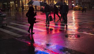 Shoppers walk in a rainstorm, Monday, Nov. 30, 2020 in New York. With people staying home as virus cases surge, Cyber Monday is expected to be the biggest online shopping day yet, bringing in nearly $13 billion in one day. (AP Photo/Mark Lennihan)