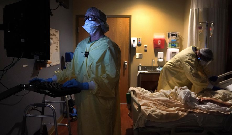 Registered nurse Shelly Girardin, left, is illuminated by the glow of a computer monitor as Dr. Shane Wilson examines COVID-19 patient Neva Azinger inside Scotland County Hospital on Tuesday, Nov. 24, 2020, in Memphis, Mo. The coronavirus pandemic largely hit urban areas first, but the autumn surge is now ravaging rural America, stressing the staffs of tiny hospitals like the one in Scotland County. (AP Photo/Jeff Roberson)