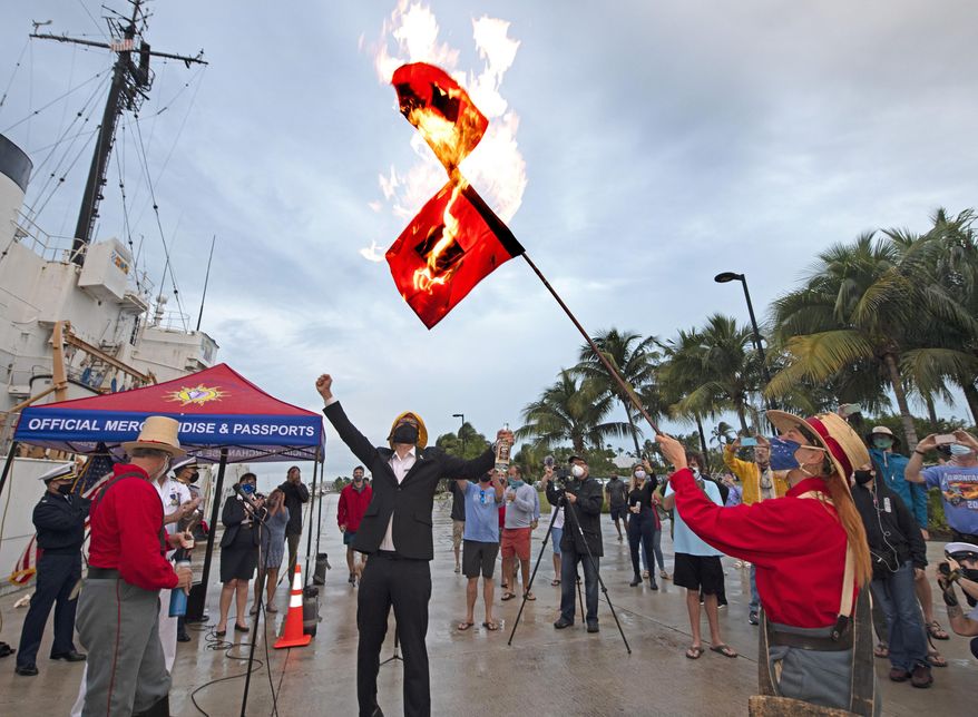 In this photo provided by the Florida Keys News Bureau, Jai Sommers holds hurricane flags as they burn after being doused with rum to mark the end of the 2020 Atlantic hurricane season, Monday, Nov. 30, 2020, in Key West, Fla. According to the National Oceanographic and Atmospheric Administration, the 2020 season spawned 30 named storms including 13 hurricanes, making it the busiest on record. The flag-burning ceremony capped the Florida Keys' Conch Republic Independence Celebration, honoring the Florida Keys island chain's colorful alter ego. (Rob O'Neal/Florida Keys News Bureau via AP)