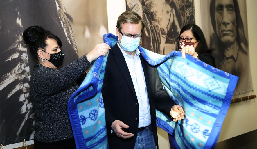 This photo provided by the Confederated Salish and Kootenai Tribes shows U.S. Attorney, Kurt Alme, center, being presented with a blanket honoring Selis, Slispe, and Ksanka people after a Confederated Salish and Kootenai Tribes Council meeting by tribal councilwoman Ellie Bundy, right, and tribal chairwoman Shelly Fyant, left, on Tuesday, Dec. 1, 2020, on the Flathead Reservation in Pablo, Mont. The Confederated Salish and Kootenai Tribes and Alme launched on Tuesday a pilot project to improve the response to the crisis of missing and murdered indigenous people. (Robert McDonald /The Confederated Salish and Kootenai Tribes via AP)