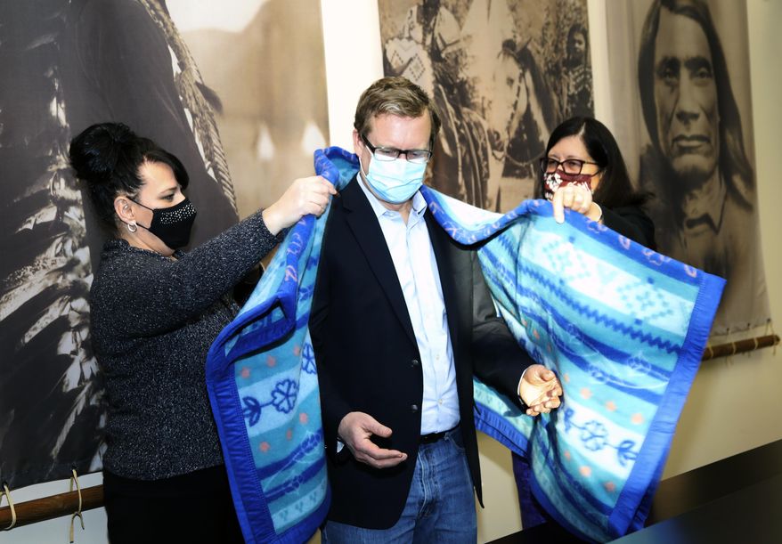 This photo provided by the Confederated Salish and Kootenai Tribes shows U.S. Attorney, Kurt Alme, center, being presented with a blanket honoring Selis, Slispe, and Ksanka people after a Confederated Salish and Kootenai Tribes Council meeting by tribal councilwoman Ellie Bundy, right, and tribal chairwoman Shelly Fyant, left, on Tuesday, Dec. 1, 2020, on the Flathead Reservation in Pablo, Mont. The Confederated Salish and Kootenai Tribes and Alme launched on Tuesday a pilot project to improve the response to the crisis of missing and murdered indigenous people. (Robert McDonald /The Confederated Salish and Kootenai Tribes via AP)