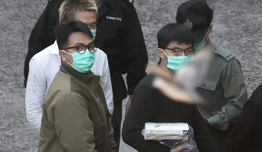 A bird flies as Hong Kong activists Joshua Wong, right, and Ivan Lam, left, are escorted by Correctional Services officers to get on a prison van before appearing in a court, in Hong Kong, Wednesday, Dec. 2, 2020. Prominent Hong Kong pro-democracy activist Wong and two other activists, Lam and Agnes Chow, were taken into custody after they pleaded guilty to charges related to a demonstration outside police headquarters during anti-government protests last year. (AP Photo/Kin Cheung)