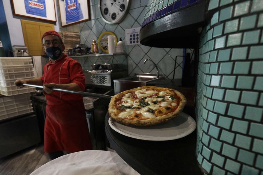 Eugenio Iorio wears a face mask to curb the spread of COVID-19 as he bakes a pizza at a restaurant in Naples, Italy, Saturday, Nov. 14, 2020. The regions of Campania and Tuscany were designated red zone on Friday, signaling the dire condition of a hospitals struggling with a surge of new admissions. (AP Photo/Gregorio Borgia)