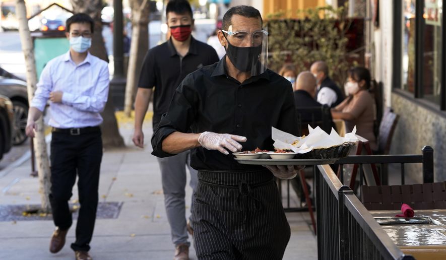 A waiter wears a mask and face covering at a restaurant with outdoor seating Tuesday, Dec. 1, 2020, in Pasadena, Calif. Pasadena has become an island in the center of the nation&#39;s most populous county, where a surge of COVID-19 cases last week led to a three-week end to outdoor dining and California&#39;s first stay-home order since the pandemic began to spread across the state in March. (AP Photo/Marcio Jose Sanchez)