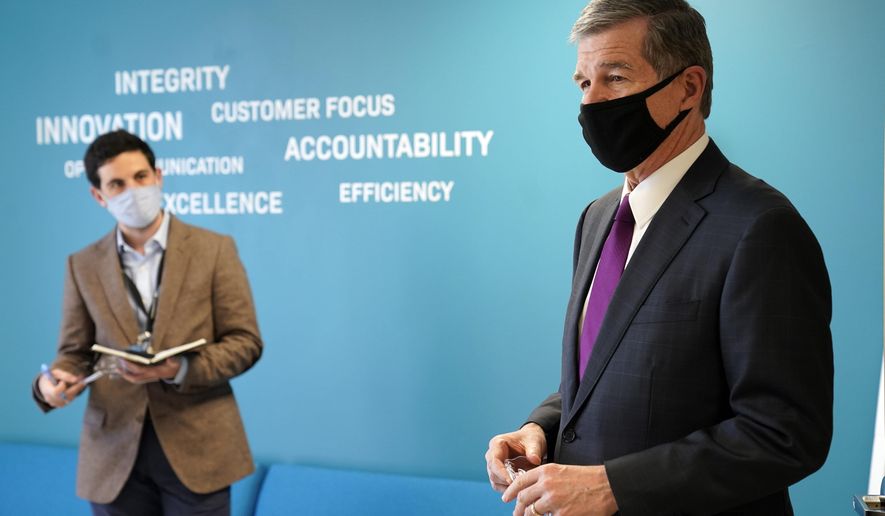 Gov. Roy Cooper, right, is seen during a visit to Gilero in Pittsboro, N.C., Thursday, Dec. 3, 2020. The medical device manufacturer began producing face shields when the pandemic started and also produces swabs for rapid tests in addition to self contained oxygenated negative pressure environments. (AP Photo/Gerry Broome)