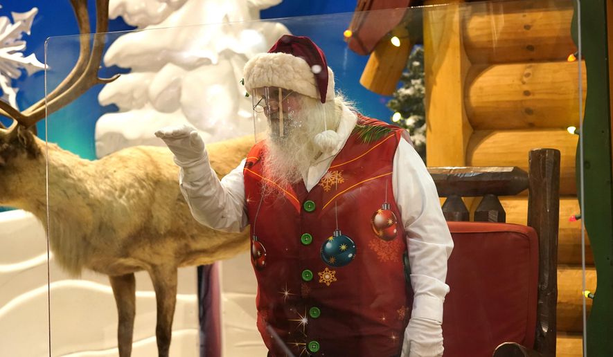Santa Claus waves at children and their families from behind a transparent barrier at Bass Pro Shops, Friday, Nov. 20, 2020, in Miami. This is Santa Claus in the Coronavirus Age, where visits are done with layers of protection or moved online. Putting hundreds of kids a day onto your lap to talk directly into your face — that&#39;s not happening. (AP Photo/Lynne Sladky)