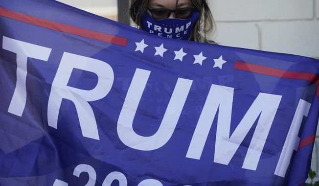In this Nov. 17, 2020, file photo, a supporter of President Donald Trump holds a flag during a news conference in Las Vegas. A state judge rejected on Friday, Dec. 4, 2020, a bid by the Donald Trump campaign to overturn the results of the Nevada election and stop the state&#x27;s six Democratic presidential electors from voting for Joe Biden. (AP Photo/John Locher, File)