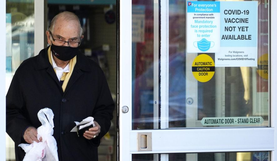 A customer wears a mask as he walks out of a Walgreen&#39;s pharmacy store and past a sign advising that a COVID-19 vaccine is not yet available at Walgreens in Northbrook, Ill., Thursday, Dec. 4, 2020. (AP Photo/Nam Y. Huh)