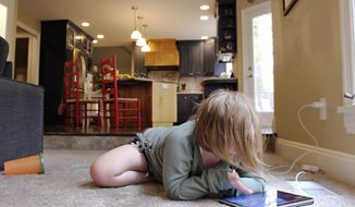 Lizzie Dale sprawls on the floor to play games on an iPad as her siblings work on school work in the kitchen behind her in their home in Lake Oswego, Ore., Oct. 30, 2020. In Oregon, one of only a handful of states that has required a partial or statewide closure of schools in the midst of the COVID-19 pandemic, parents in favor of their children returning to in-person learning have voiced their concerns and grievances using social media, petitions, letters to state officials, emotional testimonies at virtual school board meetings and on the steps of the state&#39;s Capitol. (AP Photo/Sara Cline)