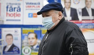 A man wearing a mask for protection against the COVID-19 infection walks by electoral posters in Bucharest, Romania, Thursday, Dec. 3, 2020. Romania will hold parliamentary elections on Sunday Dec. 6. (AP Photo/Andreea Alexandru)