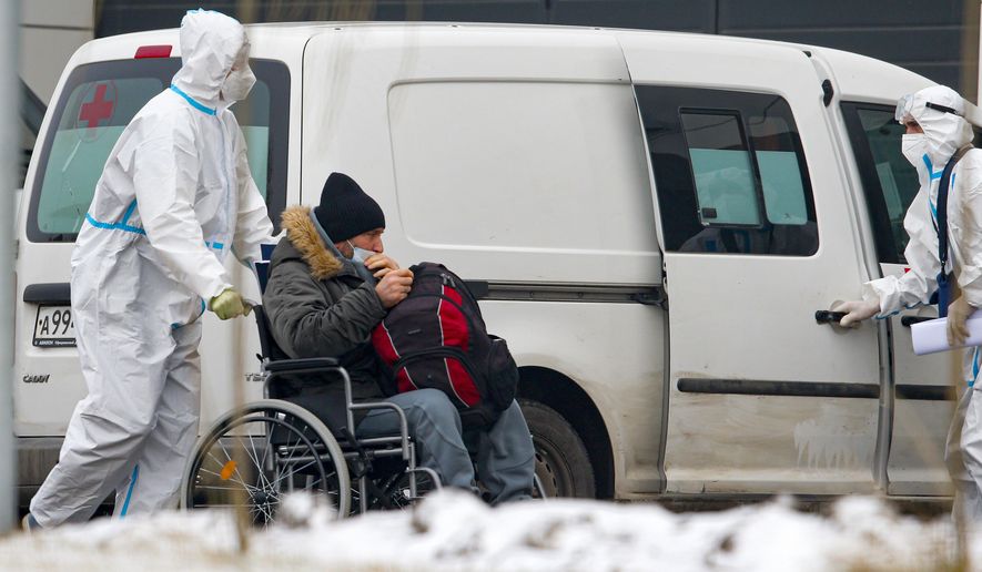 Medical workers wearing protective gear transport a patient suspected of having coronavirus in a wheelchair at a hospital in Kommunarka, outside Moscow, Russia, Thursday, Dec. 3, 2020. The country has been swept by a rapid resurgence of the outbreak this fall, with numbers of confirmed COVID-19 infections and deaths regularly hitting new highs and significantly exceeding those reported in the spring. The country&#x27;s authorities have resisted imposing a second nationwide lockdown or a widespread closure of businesses. (AP Photo/Alexander Zemlianichenko Jr)