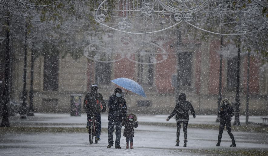 People wearing face mask protection to prevent the spread of coronavirus as snow falls in the city, in Pamplona, northern Spain, Saturday, Dec. 5, 2020. (AP Photo/Alvaro Barrientos)