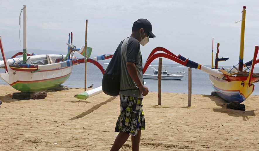 A man wearing a face mask to help curb the spread of coronavirus outbreak walks at a beach in Bali, Indonesia on Saturday, Dec. 5, 2020. (AP Photo/Firdia Lisnawati)