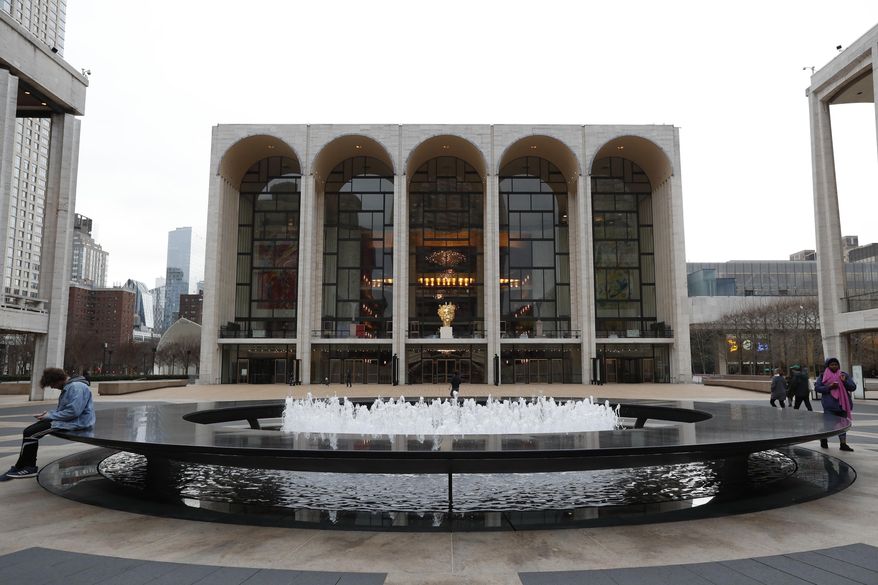 FILE - This March 12, 2020 file photo shows people by the fountain at Josie Robertson Plaza in front of The Metropolitan Opera house at Lincoln Center in New York. The shuttered Metropolitan Opera said it will lock out its stagehands in Local One of the International Alliance of Theatrical Stage Employees at midnight on Monday because it has been unable to negotiate wage cuts during the novel coronavirus pandemic. Met General Manager Peter Gelb said the company proposed 30% cuts, of which half would be restored when box office and core donations reach pre-pandemic benchmarks, as part of a five-year contract to replace the deal that expired July 31. (AP Photo/Kathy Willens, File)