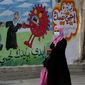 FILE - A woman walks past a mural encouraging the wearing of face masks amid the coronavirus pandemic, on the main road of Nusseirat refugee camp, central Gaza Strip, on Nov. 24, 2020. Arabic reads: &amp;quot;protect yourself, together we protect the old.&amp;quot; The prickly orb is on every news and medical site. It&#39;s all over TV and on flyers for COVID car cleaning. (AP Photo/Adel Hana, File)
