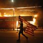 A protester carries a U.S. flag upside down as he walks past a burning building in Minneapolis on May 28, 2020, during a protest over the death of George Floyd, a Black man who died after a white Minneapolis police officer pressed a knee into his neck for several minutes. (AP Photo/Julio Cortez)