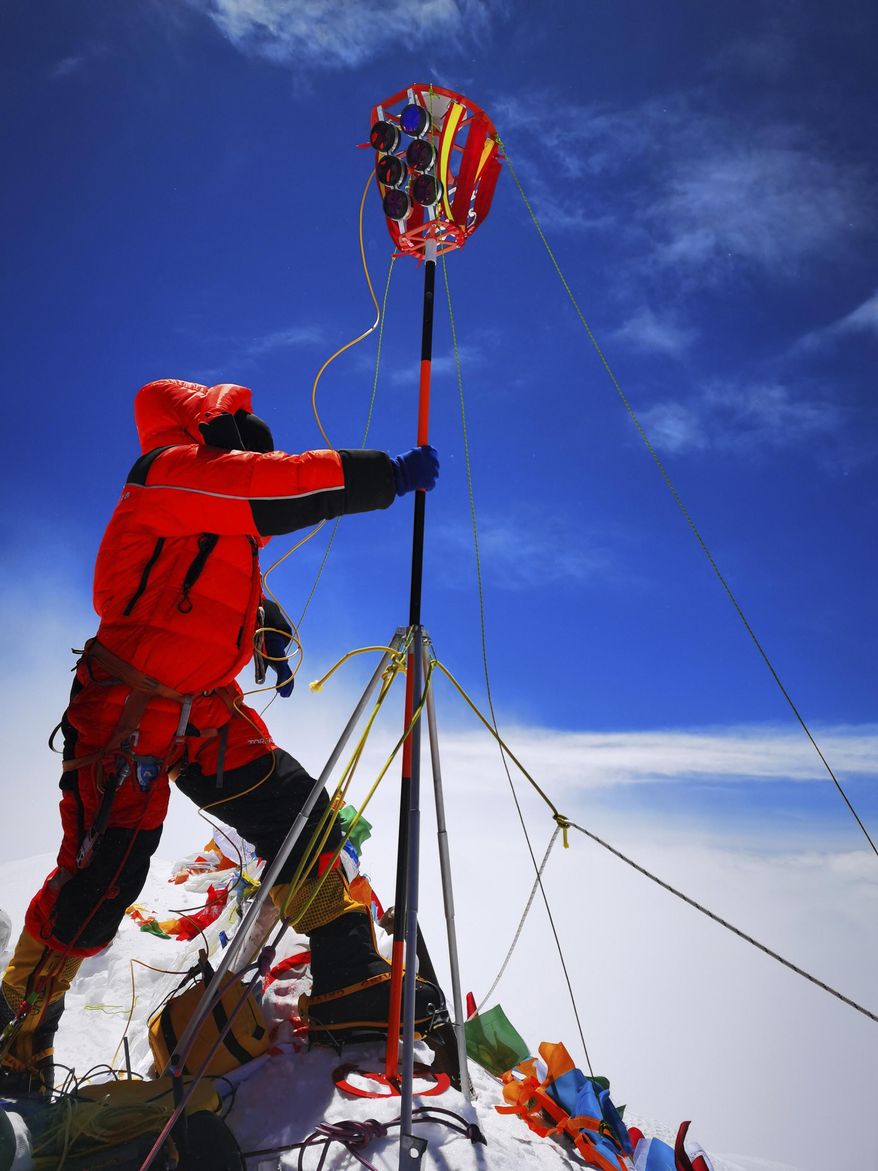 FILE - In this May 27, 2020, file photo released by Xinhua News Agency, a member of a Chinese surveying team sets up a survey equipment on the summit of Mount Everest also known locally as Mt. Qomolangma. China and Nepal have jointly announced on Tuesday, Dec. 8, 2020, a new height for Mount Everest, ending a discrepancy between the two nations. (Tashi Tsering/Xinhua via AP, File)